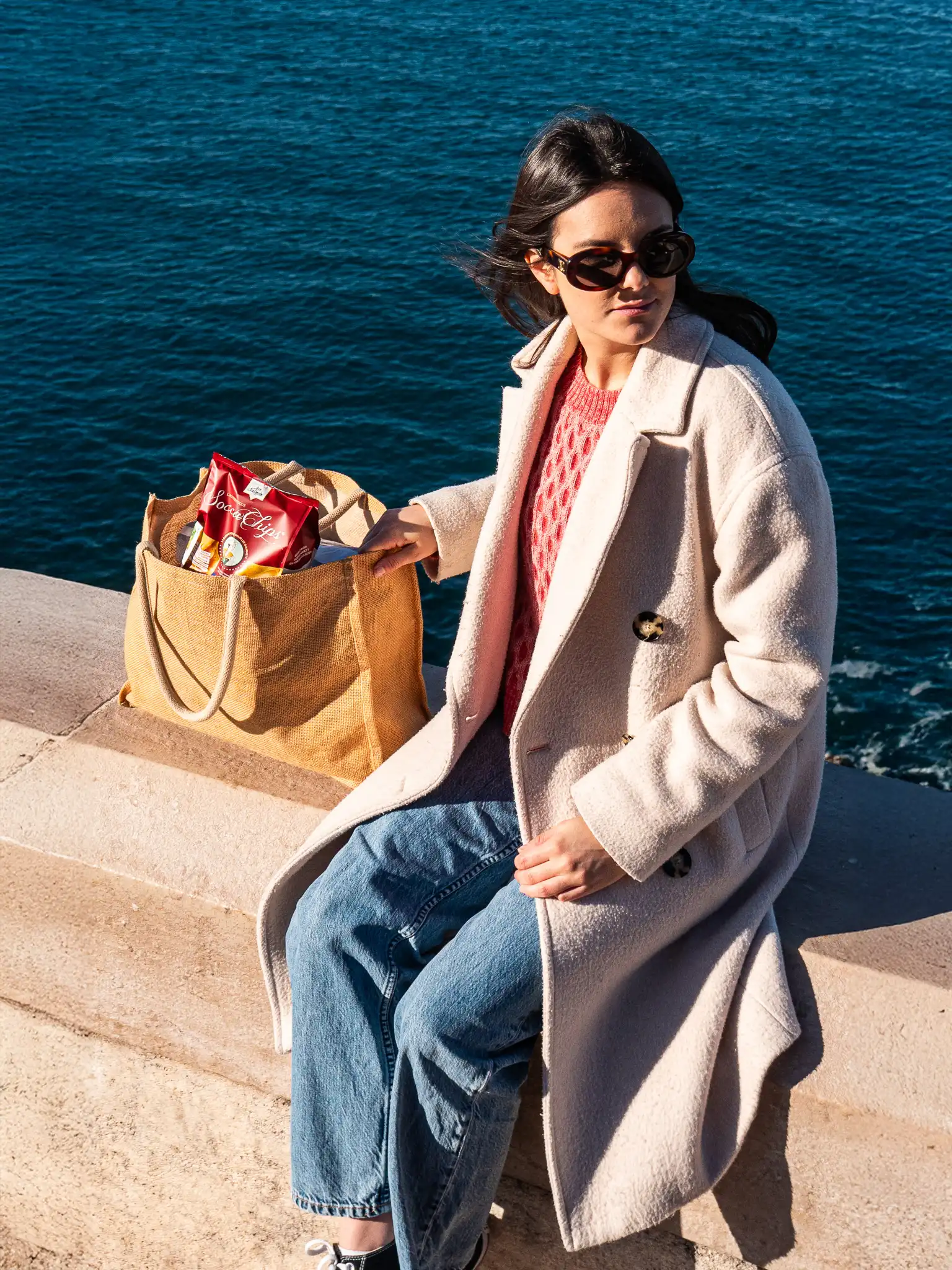 Un modèle assis sur le muret à Rauba Capeu, près de la Promenade des Anglais, avec un tote bag contenant un paquet de Socca Chips.